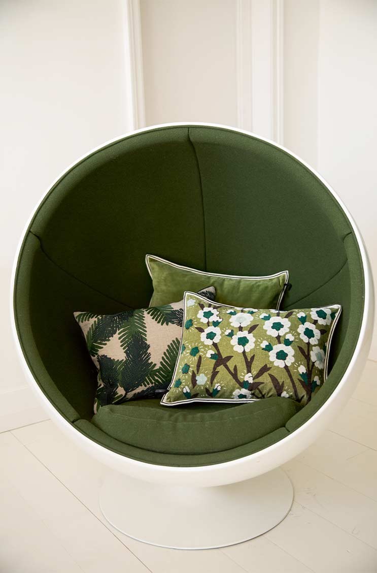 Das Moodbild zeigt grüne Kissen von Élitis auf einem dunkelgrünen Stuhl – im Onlineshop RAUM concept store