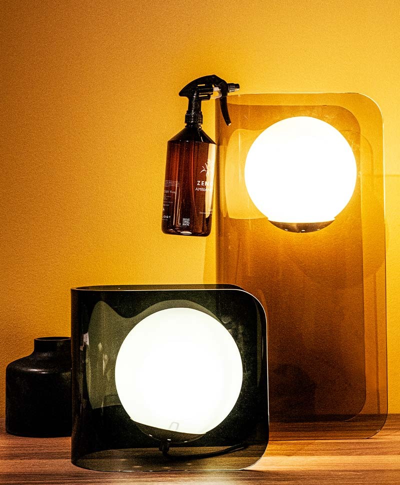 Moodbild, das einen Raumduft von Zenology zeigt, der  vor einem orangefarbenen Hintergrund dekorativ an einer Lampe hängt
