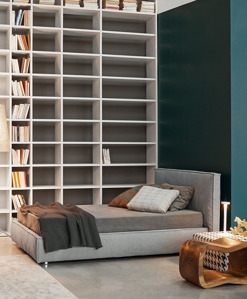 Ein graues gepolstertes Bett von Flexteam vor einem Bücherregal