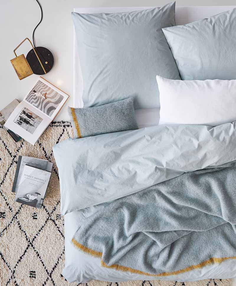 Draufsicht auf ein zerwühltes Bett mit pastellblauer Bettwäsche - auf dem Teppich daneben liegen einige aufgeschlagene Bücher und eine kleine Lampe