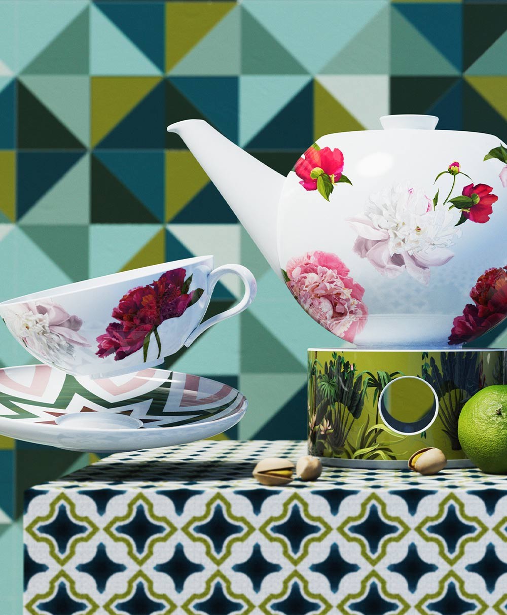 Moodbild, das die Teekanne mit Stövchen, sowie eine Teetasse mit Unterasse zeigt, die dekorativ vor einem geometrischen Hintergrund in Grüntönen arrangiert wurden