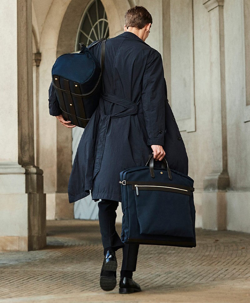 Ein Mann mit Mantel trägt die Anzugtasche und die Reisetasche von Mismo