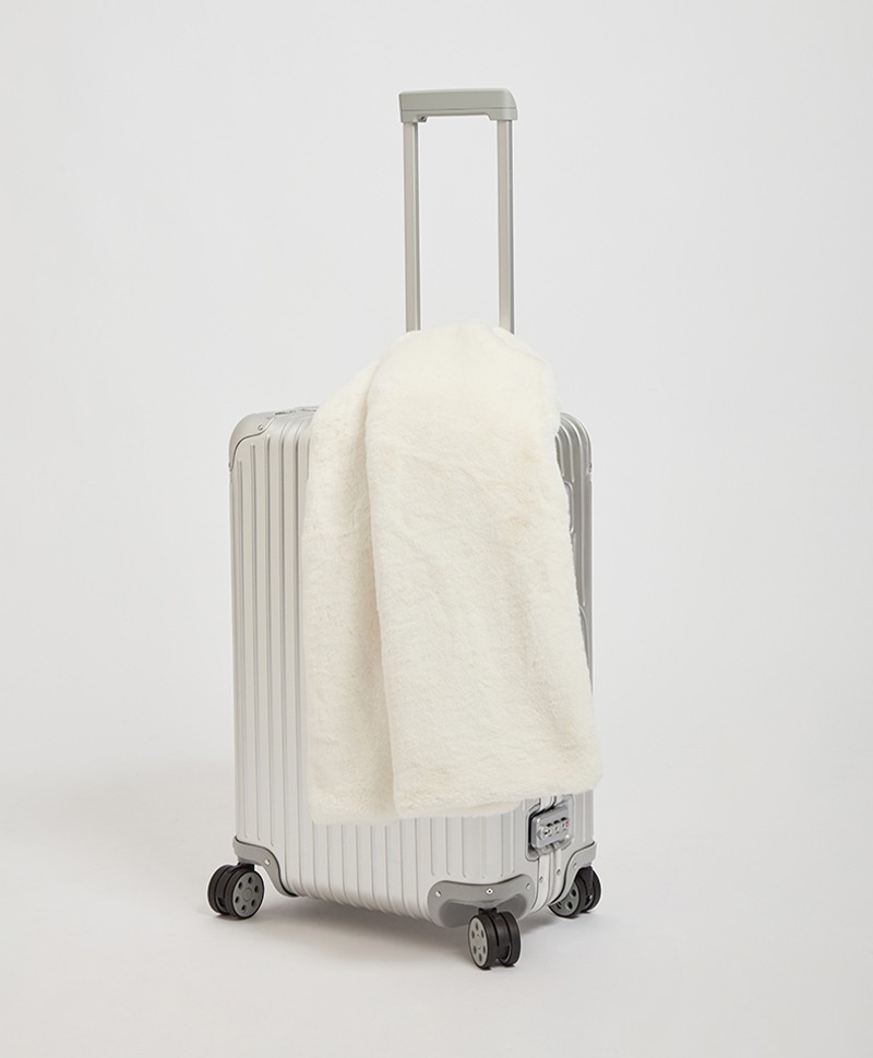 Das Moodbild zeigt die Decke Brady aus Kunstfell von der Marke Apparis in der Farbe ivory auf einem Koffer – im Onlineshop RAUM concept store