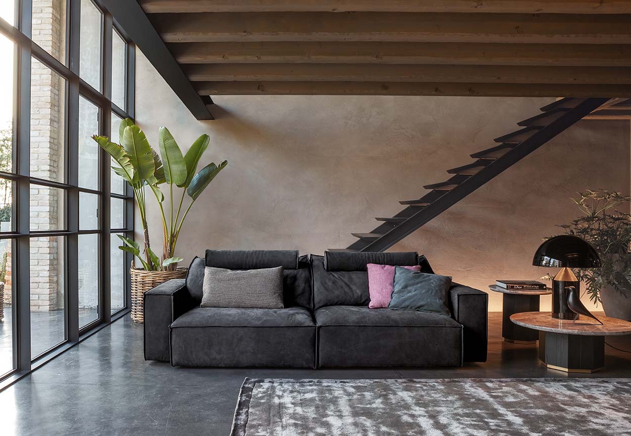 Ein anthrazites Zweisitzer Sofa von Flexteam in einem hellen Raum vor einer Treppe