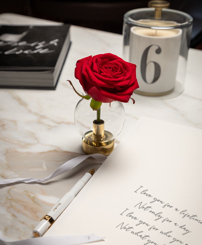 Moodfoto eines handgeschriebenen Briefes, neben dem eine Rose in einer Klong Vase steht