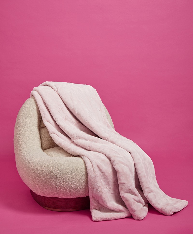 Das Moodbild zeigt die Decke Brady aus Kunstfell von der Marke Apparis in der Farbe blush auf einem weißen Sessel – im Onlineshop RAUM concept store