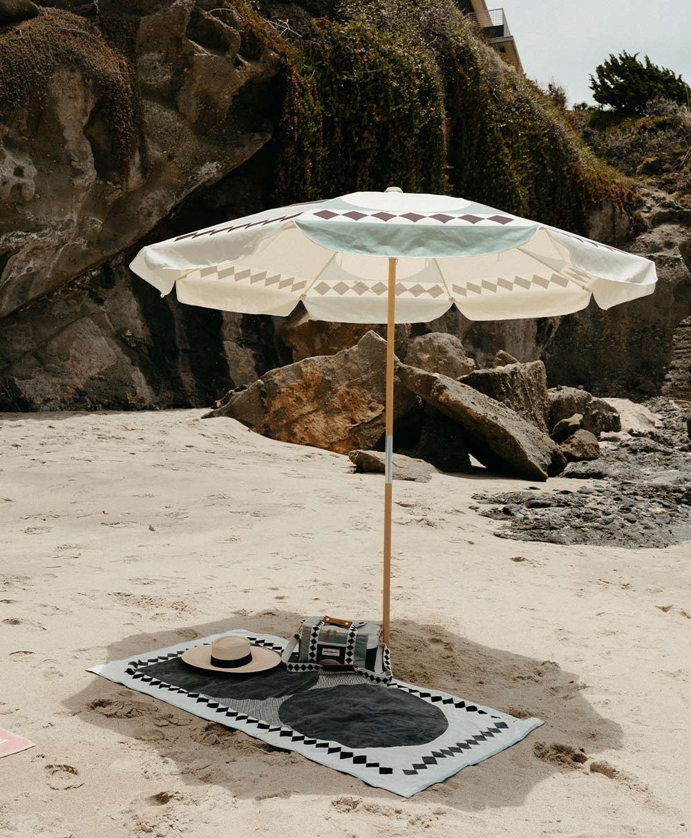 Moodbild des Strandtuchs „Beach Towel“ und des Sonnenschirms „Amalfi Beach Umbrella“ im grünen Diamond Design aus der 2023 Sommer Kollektion von Business&Pleasure im RAUM concept store.