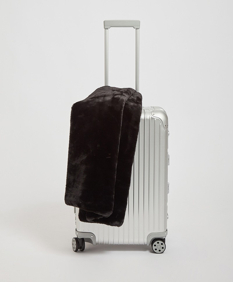 Das Moodbild zeigt die Decke Brady aus Kunstfell von der Marke Apparis in der Farbe noir auf einem Koffer – im Onlineshop RAUM concept store