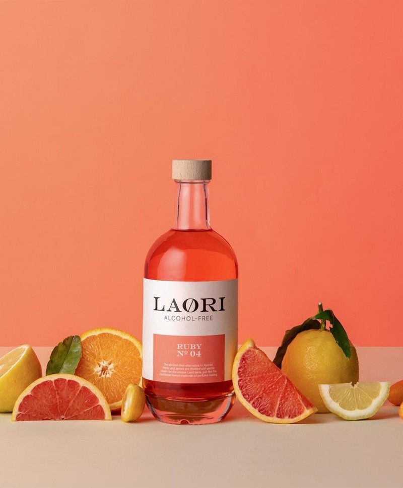 Hier sehen Sie eine 0,5l Flasche alkoholfreien Aperitif – Ruby No. 4 von der Marke LAØRI zwischen Früchten stehen – RAUM concept store