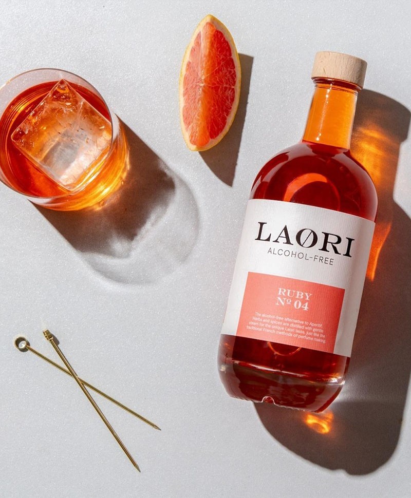 Hier sehen Sie eine 0,5l Flasche alkoholfreien Aperitif – Ruby No. 4 von der Marke LAØRI mit einem Glas und einem Grapefruit Stück – RAUM concept store