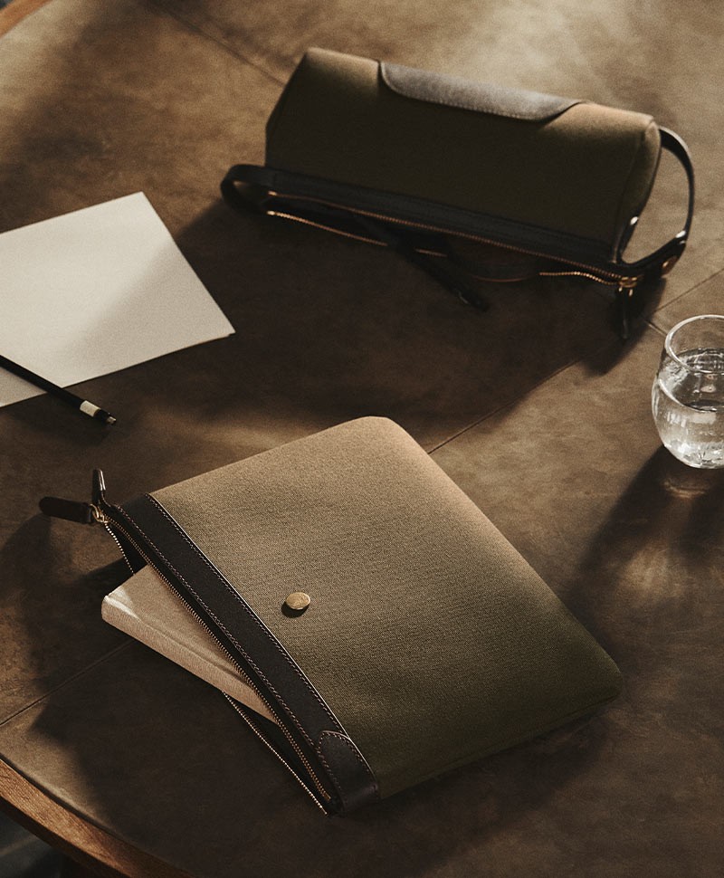Moodbild zeigt kleine olivfarbene Täschchen von Mismo zusammen mit einem Zettel und einem Wasserglas auf einem dunklen Holztisch