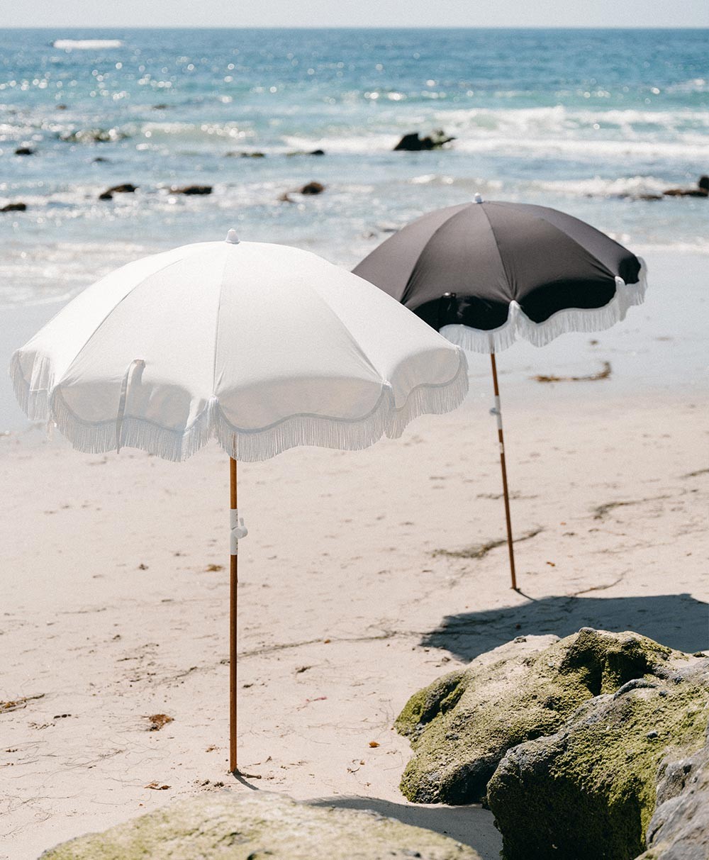 Moodbild der Sonnenschirme „Holiday Beach Umbrella“ im weißen und schwarzen Design aus der 2023 Sommer Kollektion von Business&Pleasure im RAUM concept store.
