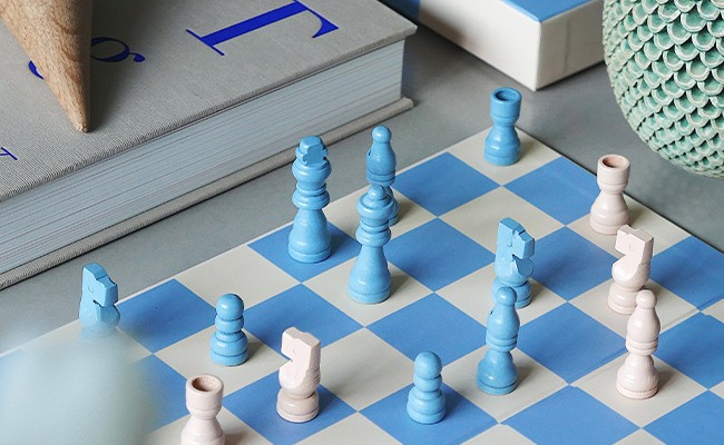 Das New Play Chessgame von Printworks wird zusammen mit einem Buch und einigen Dekoelementen in einer Nahaufnahme gezeigt
