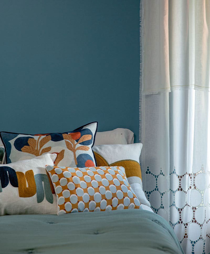 Das Moodbild zeigt verschiedene Kissen auf einem Bett von Élitis – im Onlineshop RAUM concept store