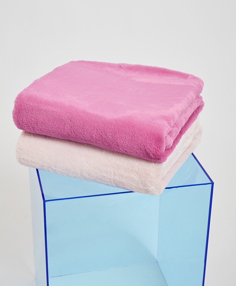 Das Moodbild zeigt die Decke Brady aus Kunstfell von der Marke Apparis in der Farbe blush und Pink auf einem blauen Hocker – im Onlineshop RAUM concept store