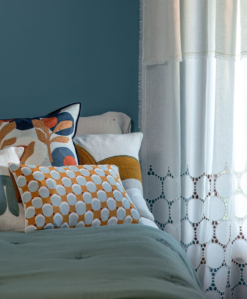 Das Moodbild zeigt verschiedene Kissen auf einem Bett und einen Vorhang von Élitis – im Onlineshop RAUM concept store